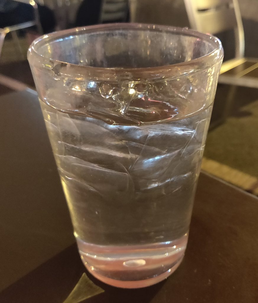 water in clear glass with light brown background - drink lots of water to achieve a flat tummy