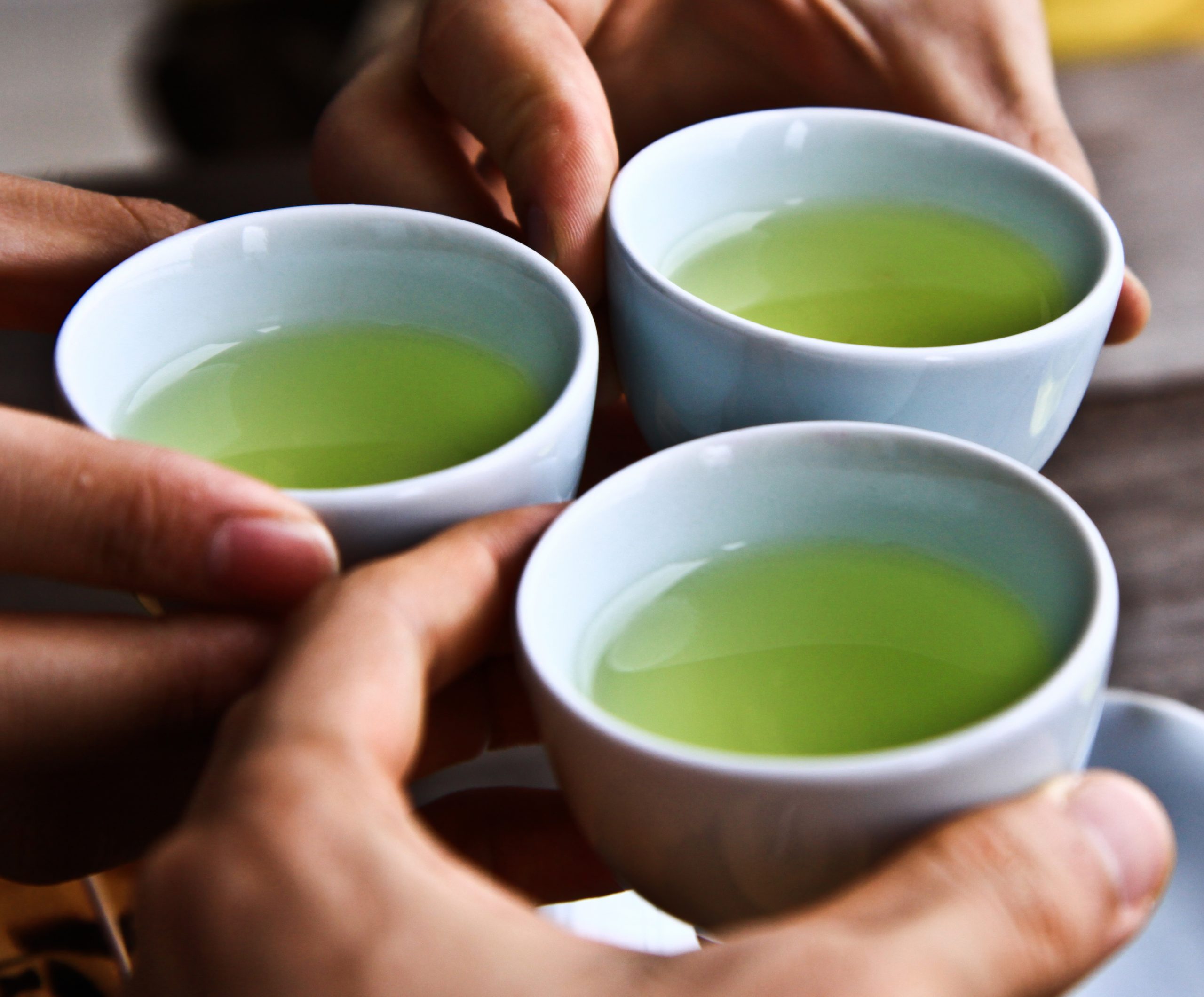 3 white cups containing clear, pale green tea - fingers of hands touching cups