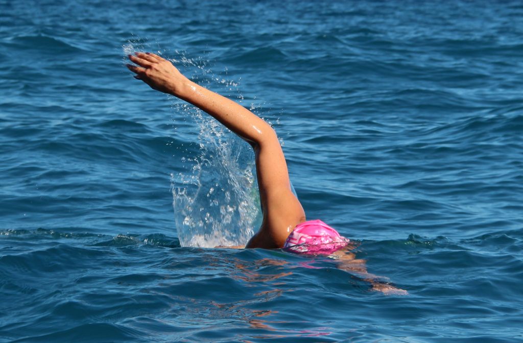 woman in a pink bathing hat swimming the crawl in blue sea