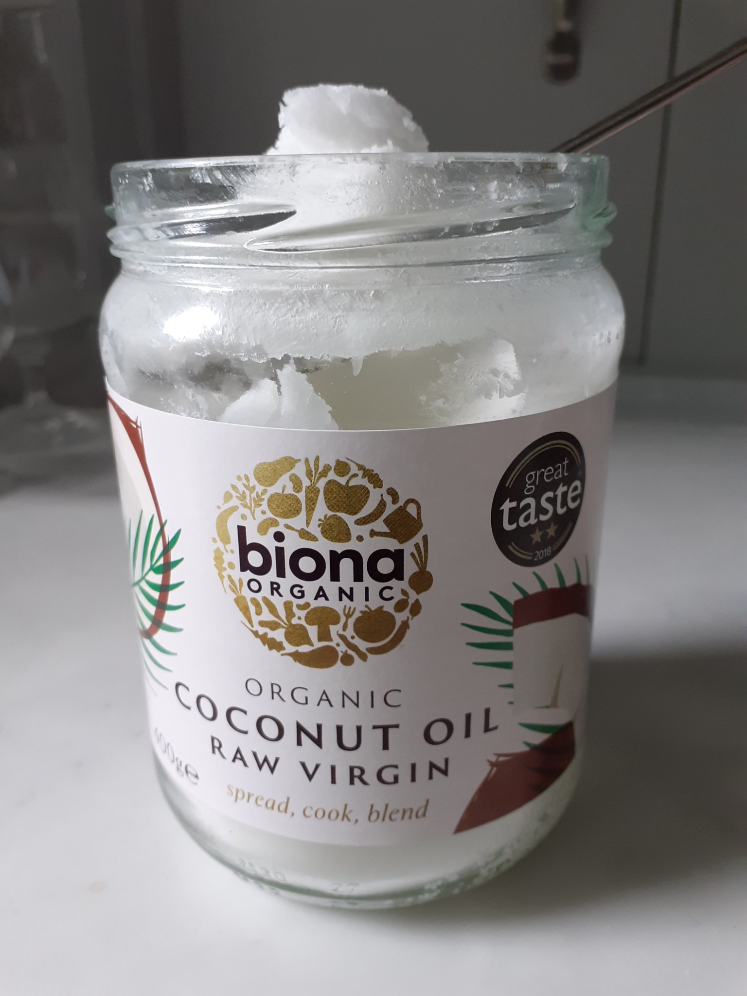 glass jar with label saying 'coconut oil raw virgin', white and creamy - on white worktop with grey background