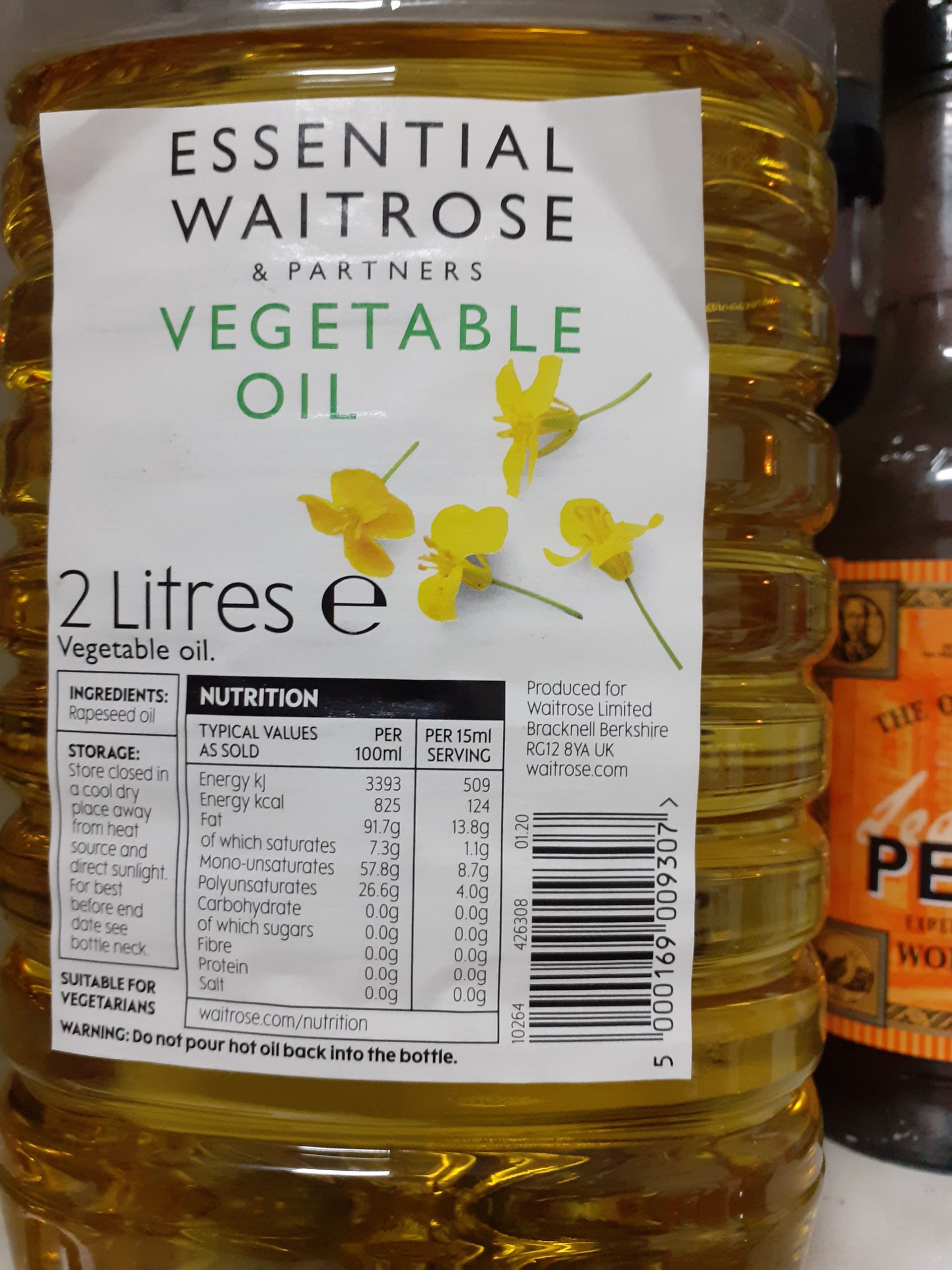 Clear plastic bottle of yellow oil, a white label with black and green print saying Vegetable Oil