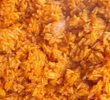 Orange-coloured grains of cooked rice with red and pink pieces of pepper and tomato