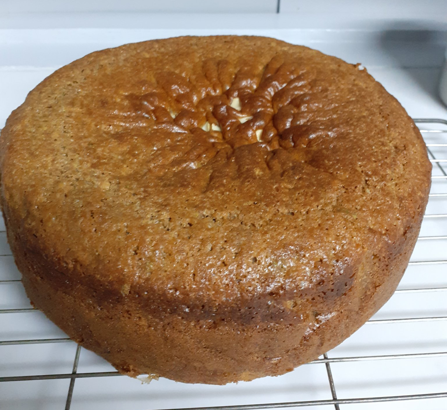 Golden brown cake with sprinkling of nuts on top, on wire cooling tray - on white worktop and blue background
