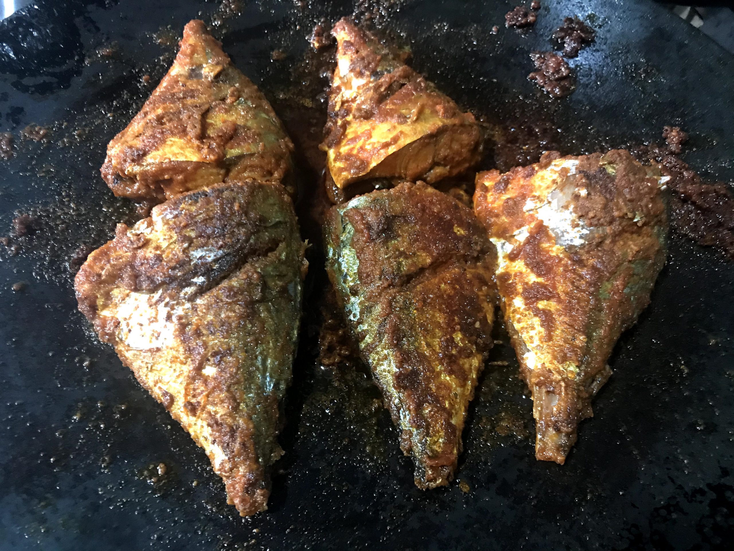 Fried mackerel, grey and silver with orange spices, in black pan