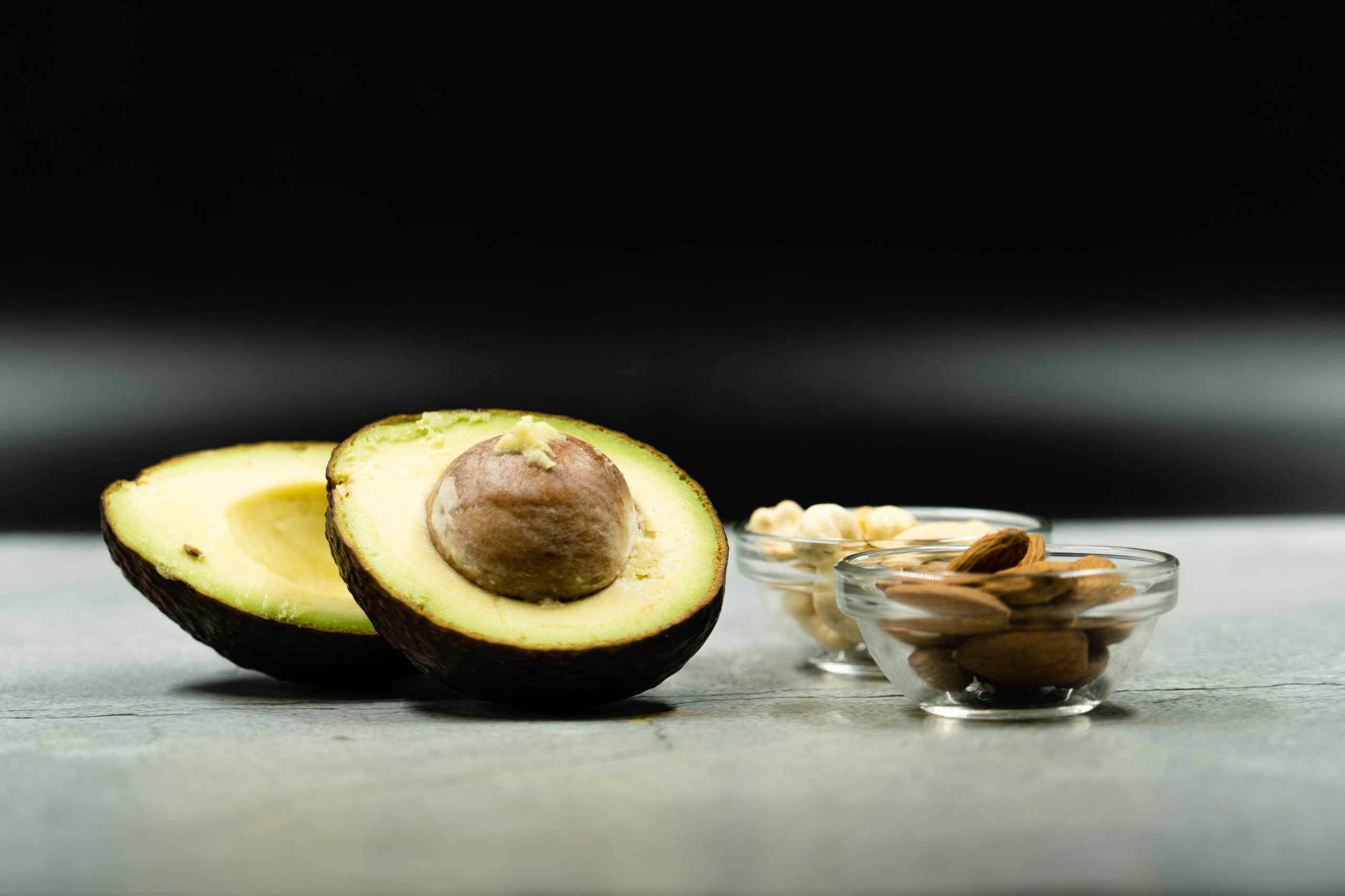 Avocado, cut in half. Bowl of nuts. On white surface with black background.