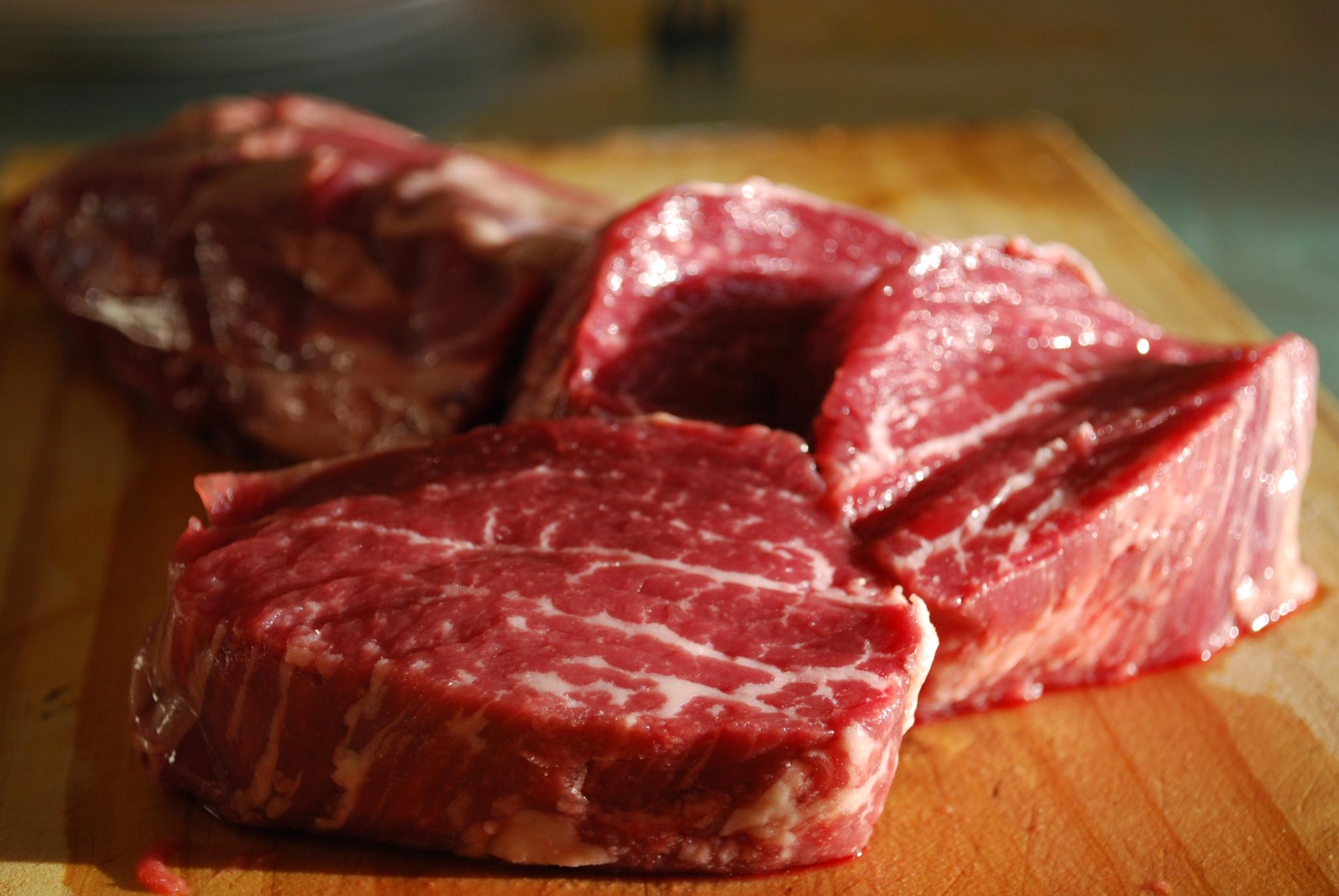 Raw steaks of beef, on wooden surface with black background.